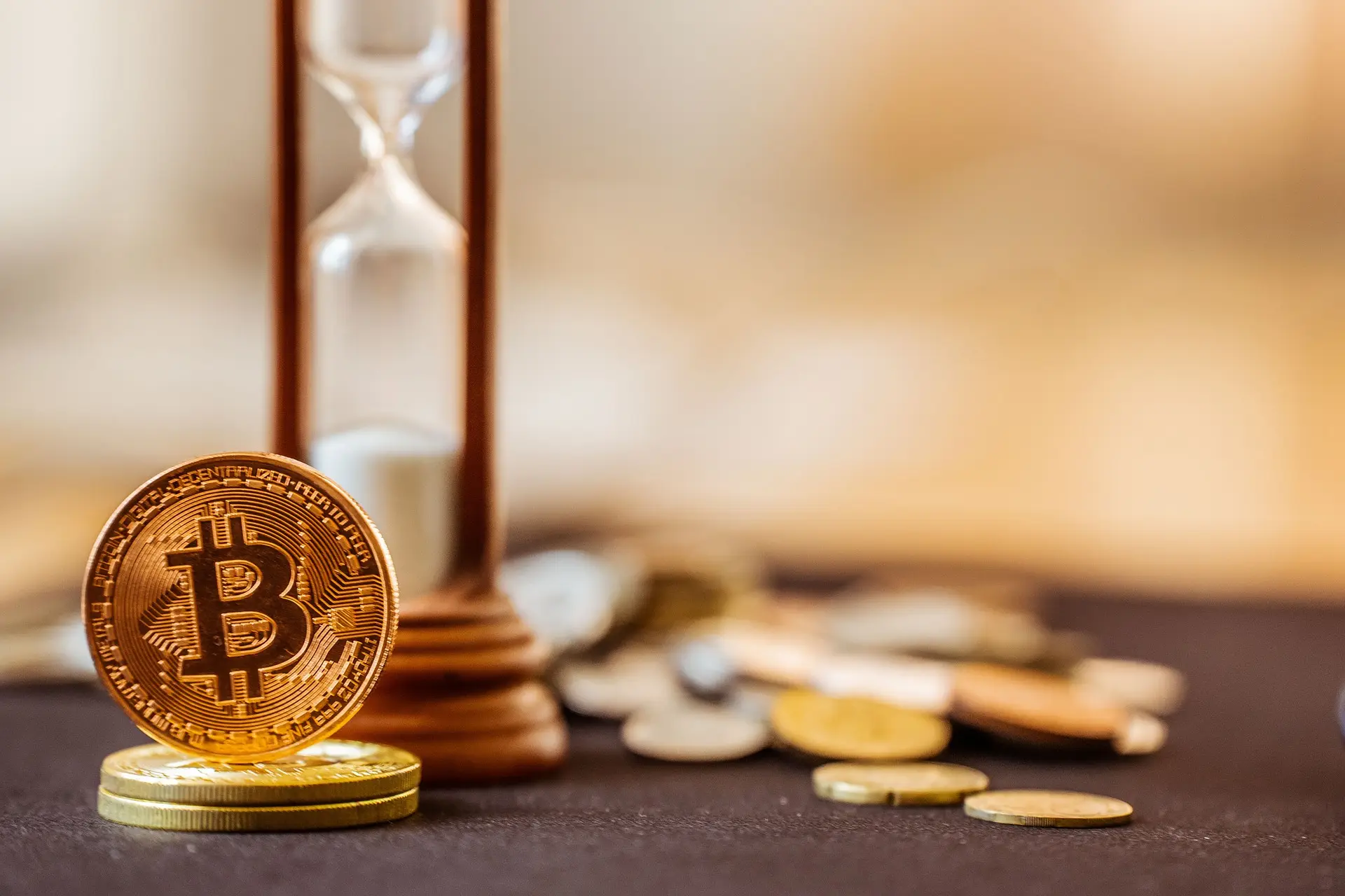 A bitcoin token standing beside an hourglass, with loose coins in the background