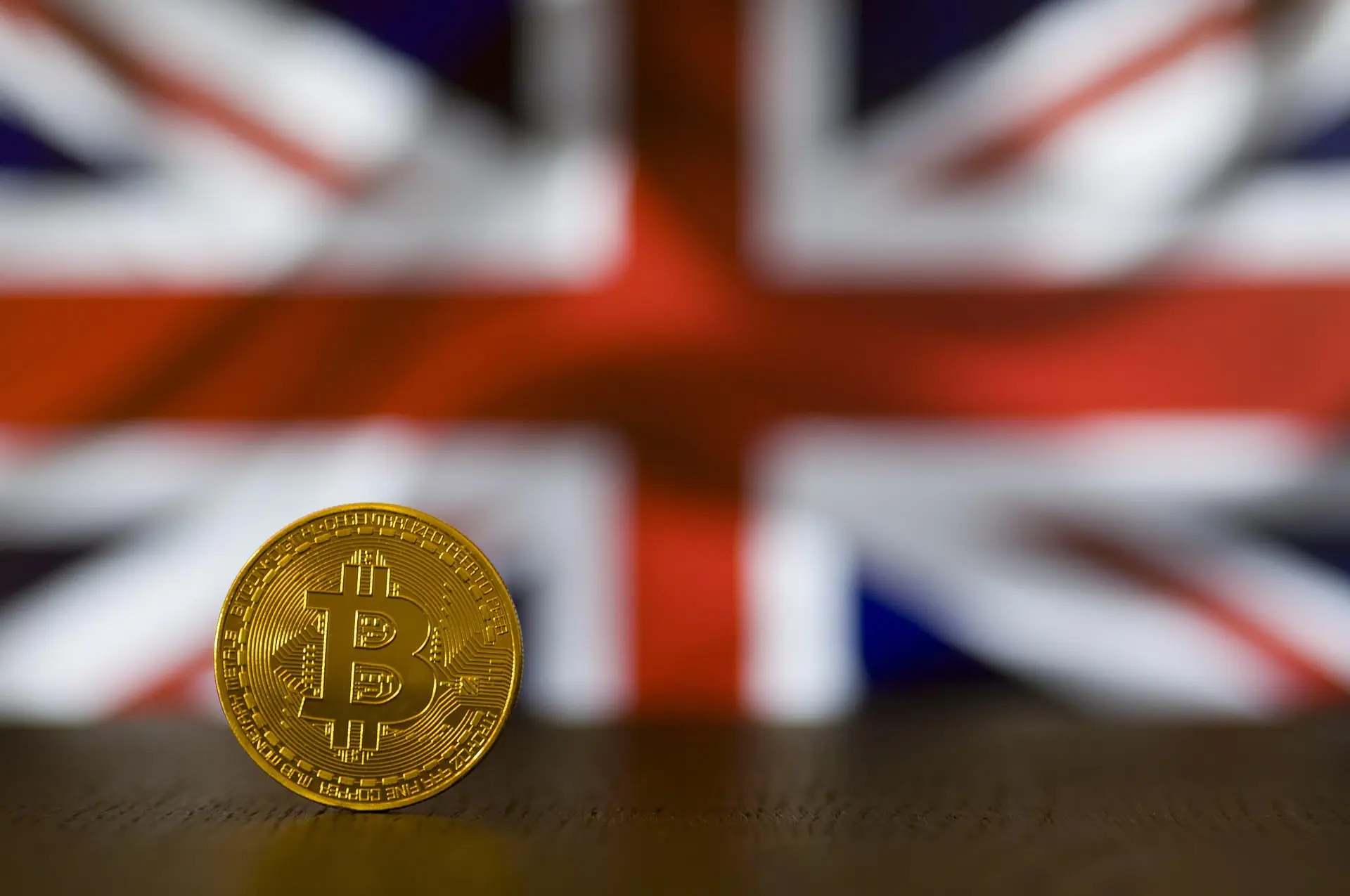 A bitcoin coin standing upright in front of a blurred Union Jack flag