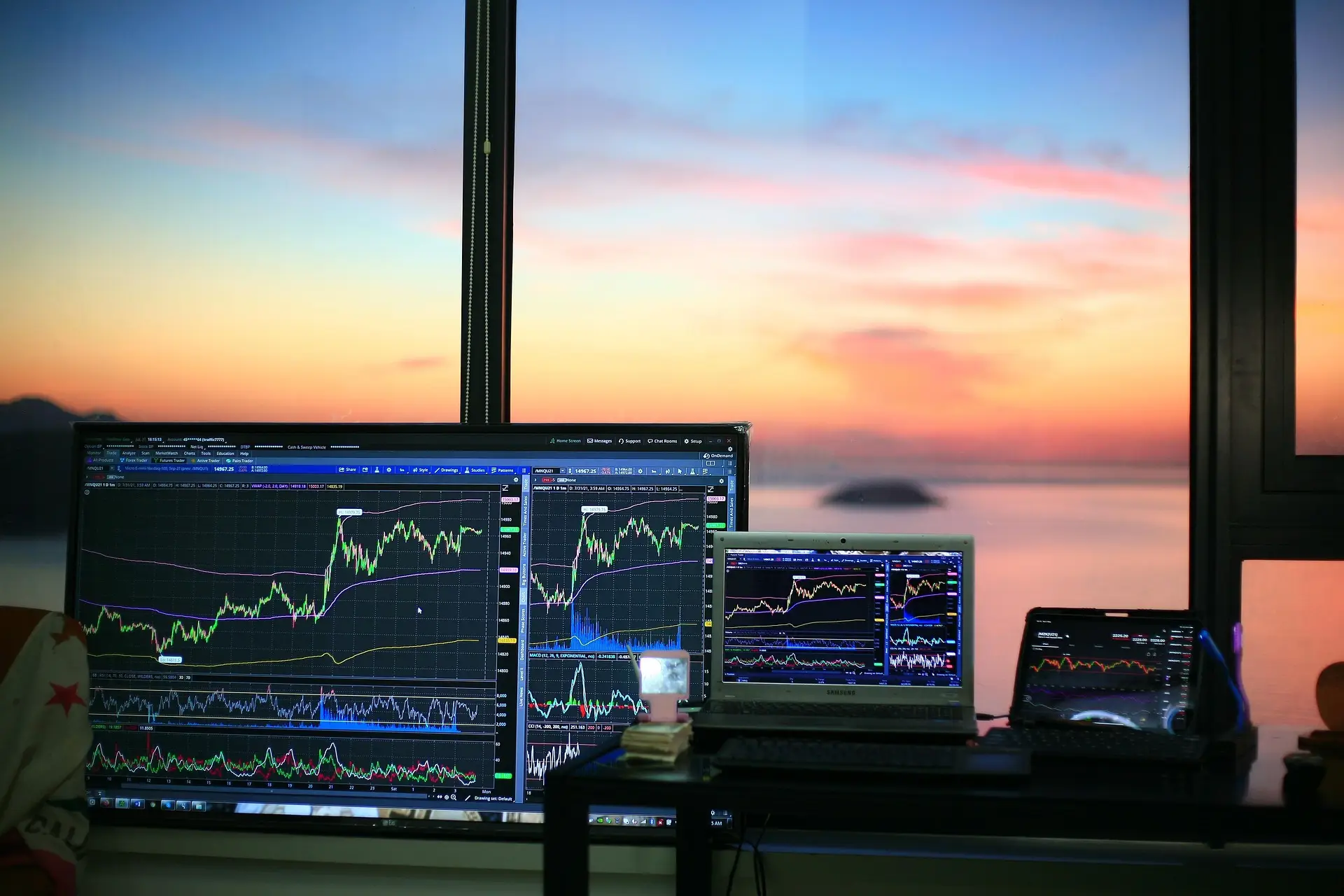 A trading desk at dusk with several screens showing candlestick charts moving in both directions