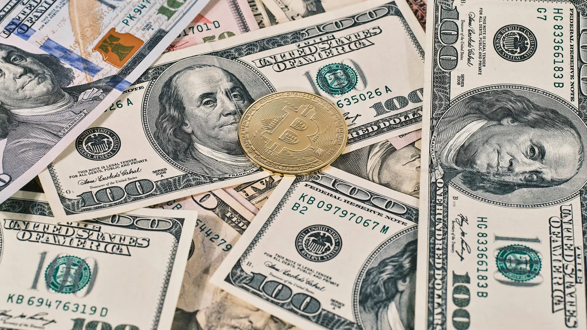 A bitcoin token resting on a spread of one hundred dollar notes